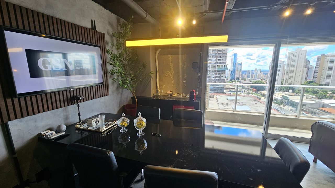 Sala de reuniões com TV exibindo a marca GSN e vista panorâmica de Goiânia